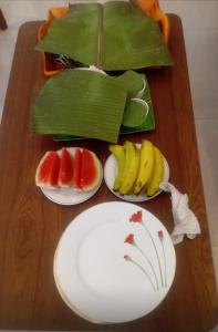 a wooden table with plates of fruit and a banana at Arches View Home Stay in Ella +22 photos