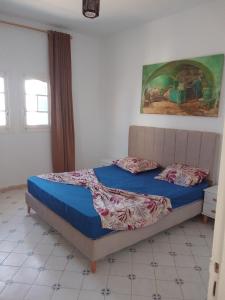 a bedroom with a bed with blue sheets and a painting at Taguermess 1 in Djerba