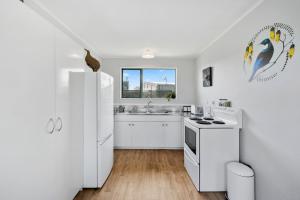 a white kitchen with a sink and a refrigerator at Restful on Rutherford - Waikanae Holiday Home in Waikanae