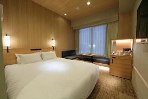 a hotel room with a large white bed and a chair at Candeo Hotels Kobe Tor Road in Kobe