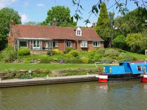 a house with a boat docked in the water at Waterside Cottage - Sleeps 11 on Grand Union Canal in Linslade
