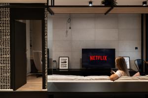 eine Frau, die auf einem Bett vor einem Fernseher sitzt in der Unterkunft Kraków Wawrzyńca Suites by Downtown Apartments in Krakau