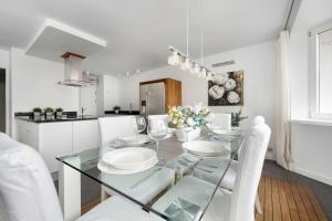 a white kitchen with a glass table and white chairs at Family Apartment with 3 Bedrooms & Air Conditioning in the Centre of Wrocław by Noclegi Renters in Wrocław