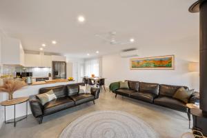 a living room with leather couches and a kitchen at Chrissie's Cottage in Dunsborough