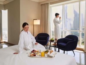 a woman in a hotel room with a tray of food at Fairmont Dubai in Dubai