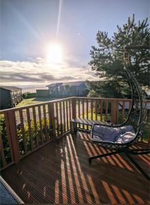 a bench on a deck with the sun behind it at 42 pine lodge & sea views in Llanarmon