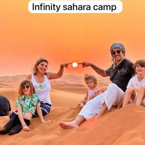 メルズーガにあるInfinity sahara campの砂漠の砂の上に座っている家族