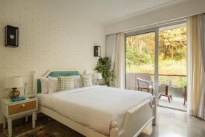 a white bedroom with a bed and a balcony at Da Alohas Hibiscus Oasis Pool Facing Candolim in Betim