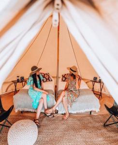 Dos mujeres sentadas en camas en una tienda de campaña. en Bryce Canyon Escalante Glamping, en Cannonville