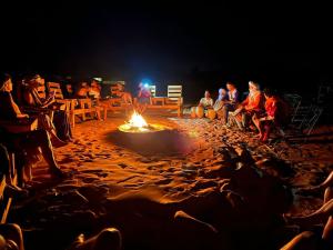 a group of people sitting around a fire on the beach at Oasis Desert Luxury Camp in Merzouga
