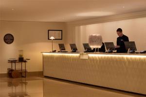 a man standing at a reception desk with laptops at The May Fair, A Radisson Collection Hotel, Mayfair London in London