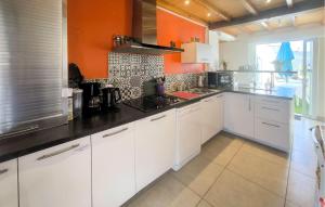 a kitchen with white cabinets and an orange wall at Maison Près De La Mer in LʼAiguillon-sur-Mer