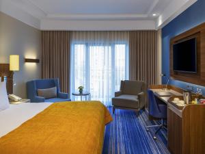 a hotel room with a bed and chairs and a television at Mövenpick Hotel Istanbul Asia Airport in Istanbul