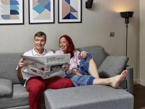 um homem e uma mulher sentados em um sofá segurando uma caixa em Aparthotel Adagio Paris Suresnes Longchamp em Suresnes