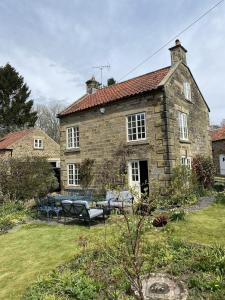 an old stone house with tables and chairs in a yard at Holly Cottage in Hutton le Hole