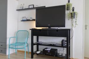 une télévision sur un meuble TV avec une chaise bleue dans l'établissement Inselblume 37 - Ferienwohnung mit Meerblick im Stranddistelweg 58, à Burgtiefe auf Fehmarn 