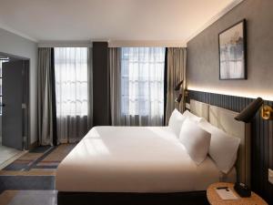 a hotel room with a large white bed and windows at The Sebel Sydney Martin Place in Sydney