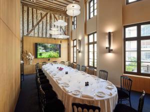 une longue table de banquet dans une pièce avec des fenêtres dans l'établissement Domaine de la Reine Margot Paris-Issy - MGallery Collection, à Issy-les-Moulineaux
