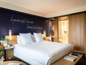 - une chambre dotée d'un grand lit blanc et d'un mur avec un bureau dans l'établissement Domaine de la Reine Margot Paris-Issy - MGallery Collection, à Issy-les-Moulineaux
