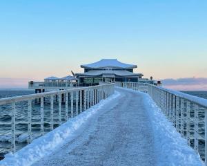 une jetée couverte de neige avec un bâtiment sur l'eau dans l'établissement Grand Hotel Seeschlösschen Sea Retreat & SPA, à Timmendorfer Strand 85 autres photos