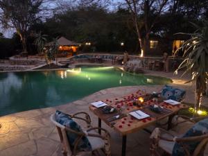 a table and chairs in front of a pool at night at Dolly Farm & River Camp, Luxury Tents in Usa River +25 photos