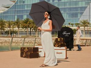 Una mujer sosteniendo un paraguas junto a un equipaje. en Fairmont Doha, en Doha