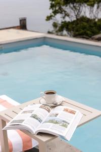 une tasse de café et un livre sur une table près d'une piscine dans l'établissement BIOMA Adega - Escala Gourmet, à Calheta de Nesquim