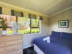 a bedroom with a bed with a fan and a window at Seashell Cottage Hahei in Hahei
