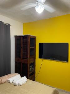 une chambre avec un mur jaune avec une télévision à écran plat dans l'établissement Loft da Praia dos Corais, à Cabo Frio