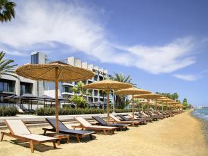 une rangée de chaises et de parasols sur une plage dans l'établissement Mercure Larnaca Beach Resort, à Larnaka