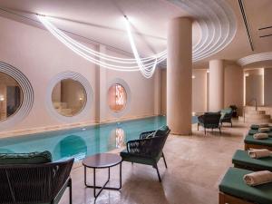 een zwembad in een kamer met stoelen en een tafel bij Swissôtel Tbilisi in Tbilisi City