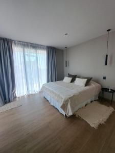 a white bedroom with a large bed and large windows at ENTREVID suites & spa in Anchoris