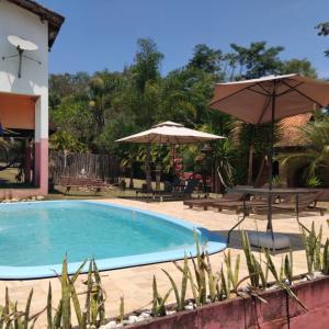 une piscine avec deux parasols et une table dans l'établissement Nosso Recanto Gaúcho Paraíso no interior Guaratinguetá Aparecida, à Guaratinguetá