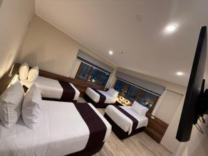 a hotel room with three beds and two windows at Hotel Andesmar Huancayo in Huancayo