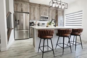 a kitchen with a refrigerator and two bar stools at Chappelle with AC King Beds Fenced Yard Garage in Edmonton