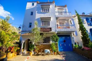 a white apartment building with a blue door and chairs at Maison d'hôte Bousaid in Chefchaouene