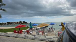 a group of tables and chairs with umbrellas on the beach at Guest House Flor de Laranjeira in São Pedro da Aldeia