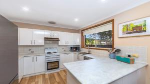 a kitchen with white cabinets and a large window at Gwendolen Cottage - Umina Beach in Ettalong Beach