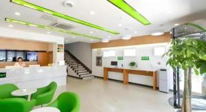a woman sitting at a desk in a office with green chairs at Vatica JiangsuJianguo Road Xuanwu Market Hotel in Xuzhou