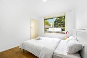 a white bedroom with a bed and a window at Comfy Croydon Family Getaway Near Trails and Cafes in Ringwood North