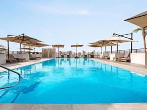 a large swimming pool with chairs and umbrellas at Novotel Dubai Gold District in Dubai