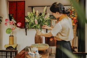 une femme disposant un vase de fleurs dans une pièce dans l'établissement Hue Memories Signature, à Thôn Trường Giang