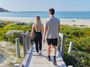 a man and woman walking down a boardwalk to the beach at Pullman Bunker Bay Resort Margaret River in Dunsborough