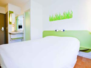 a bedroom with a white bed with a green headboard at ibis budget Metz Technopole in Metz