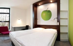 a bedroom with a bed with a green apple on the wall at 7THINGS - my basic hotel in Bremen