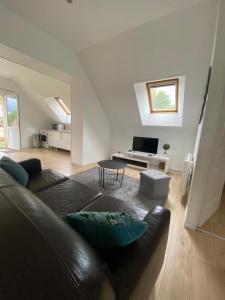 a living room with a black leather couch and a television at Au bonheur des Anes - Gite Maya in Le Quesnoy-en-Santerre