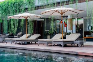 een groep stoelen en parasols naast een zwembad bij THE MUSE Pantai Nyanyi Villa in Canggu