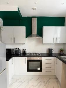 a kitchen with white cabinets and a green wall at D&D Emerald House Anfield in Liverpool