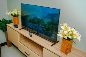 a flat screen tv on a dresser with flowers in vases at BougainVille in Fort Portal