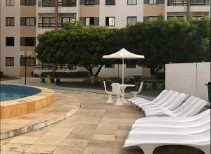 a group of white chairs and an umbrella next to a pool at Appartement mon chéri à 200 de la plage in Caucaia